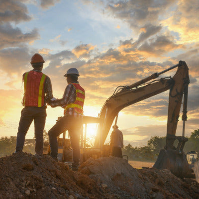 Image of two construction workers in front of heavy machinery